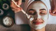 A cosmetologist meticulously applies a moisturizing mask to a young, relaxed, and smiling woman in a spa salon. The close-up portrait showcases the girl client receiving a beauty procedure from the sk