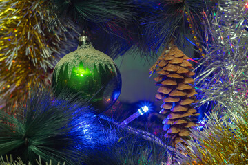 Green ball and fir cone on a Christmas tree with sparkles and tinsel.