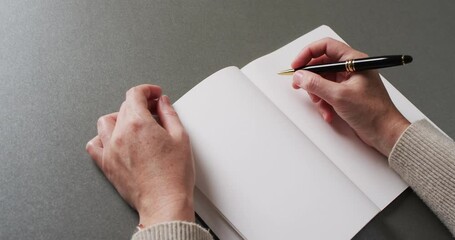 Canvas Print - Close up of hands writing with pen on book with copy space on gray background in slow motion