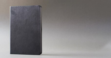 Wall Mural - Close up of closed black book standing vertical with copy space on gray background in slow motion