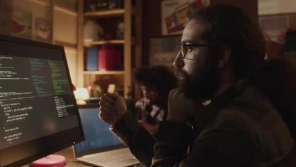 Waist up shot of long haired bearded Middle Eastern programmer examining program code appearing on black background at computer display
