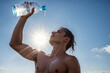 Thirsty man in a sweat pouring water from plastic bottle on himself because of hotness over blue sky