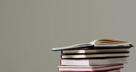 Poster - Close up of open book on stack of books on grey background, in slow motion