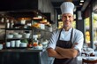 © Chand Abdurrafy - skilled Caucasian middle-aged male chef, wearing a chef's hat and apron, confidently standing in a restaurant kitchen with crossed arms, exuding competence and smiling.