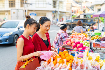 Wall Mural - Happy Asian family celebration Chinese Lunar New Year festival together. Mother and daughter choosing and buying fresh fruit orange for celebrating Chinese New Year at Chinatown street market.