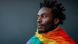© AdriFerrer - A thoughtful man with dreadlocks, draped in a rainbow flag on a dark background.