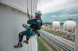 © chitsanupong - Focus top view male worker down height tank roof rope access safety inspection of thickness storage tank gas