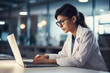 Serious female doctor using laptop and writing notes in medical journal sitting at desk at office