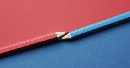 Wall Mural - Overhead view of blue and red crayons arranged on red and blue background, in slow motion