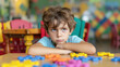 © Maryna - A brooding lonely upset boy in kindergarten is sitting alone at a desk with colored puzzles. Inability to communicate socially. Antisocial children with autism syndrome