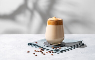 Wall Mural - Dalgona coffee. Whipped instant coffee in a glass with beans and shadow on a light background.