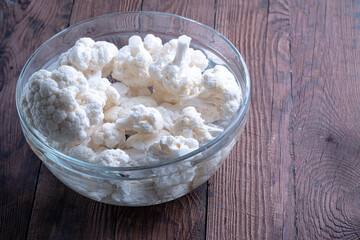 Wall Mural - Cauliflower inflorescences in a glass cup with water. Cauliflower background. Cauliflower on a wooden table.