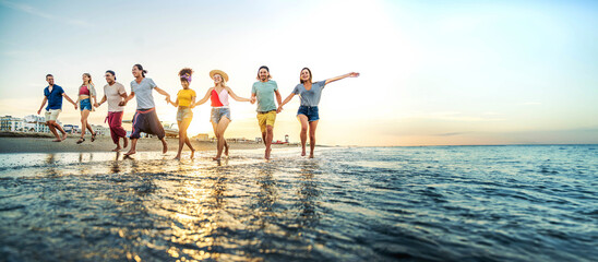 Wall Mural - Crowd of friends running to sunset sea - Summer holidays concept with guys and girls enjoying beach sunrise - Happy young people with arms up standing on coastline - Colorful background photo