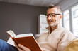 © contrastwerkstatt - Senior Man with Glasses Relaxing on Sofa, Reading a Book