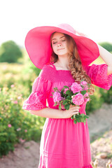 Canvas Print - Stylish teenage girl 15-16 year old wearing pink hat and dress holding roses in meadow outdoor. Spring season.