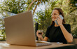 © Friends Stock - Smiling woman manager talking with client and work on laptop in cafe terrace. Distance work concept