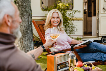 Wall Mural - Senior married caucasian couple toasting with glasses of wine with their motor home behind, traveling together by trailer camper van, caravanning on mobile home