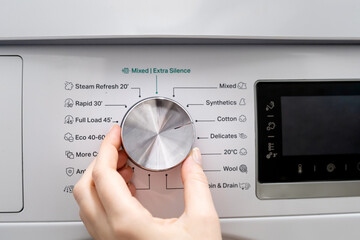 woman hand choosing program on automatic washing machine for laundry at home. turning knob on contro