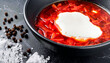 macro photo of borscht with sour cream in a black pot, peppercorns and sea salt on a black m