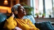 © Maryna - senior African American woman sit on the sofa, listen music with headphones