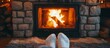 Adult feet in white socks near a small fire in a stone gas fireplace with a wooden mantle.