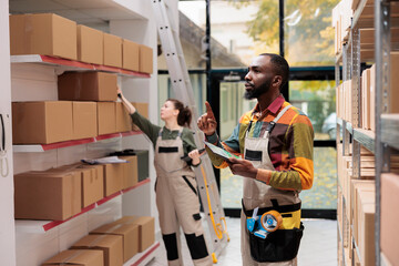 Wall Mural - Warehouse manager looking at carton boxes, checking products inventory on tablet computer. Storage room employee wearing industrial overall working at delivery in storehouse.