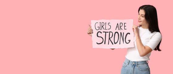 Wall Mural - Young woman holding paper with slogan GIRLS ARE STRONG on pink background with space for text. Feminism concept