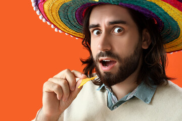 Canvas Print - Surprised young Mexican man in sombrero eating nachos on orange background