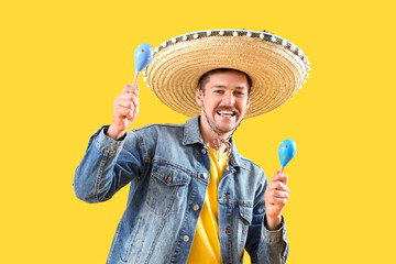 Poster - Happy young Mexican man in sombrero and with maracas on yellow background