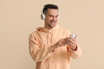 Wall Mural - Happy young man in headphones using mobile phone on beige background