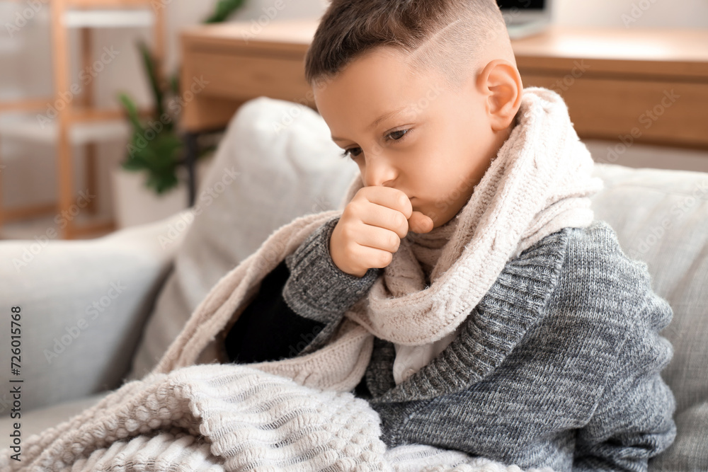 Ill little boy with scarf coughing on sofa at home, closeup