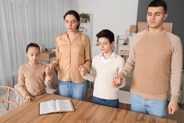 Wall Mural - Family praying together with Holy Bible on table at home
