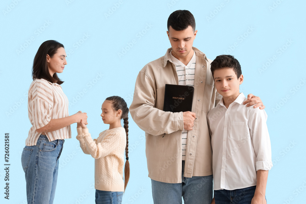Family with Holy Bible praying together on blue background