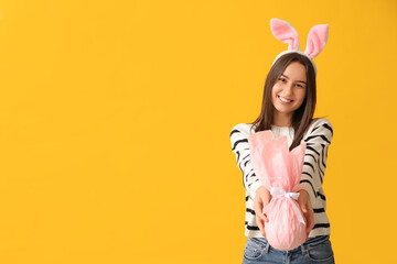 Canvas Print - Pretty young woman with bunny ears and Easter gift on yellow background