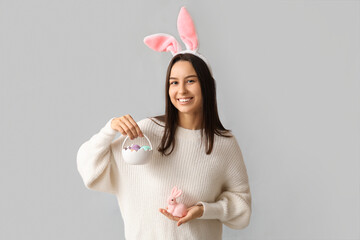 Poster - Pretty young woman with bunny ears, toy rabbit and Easter basket on grey background