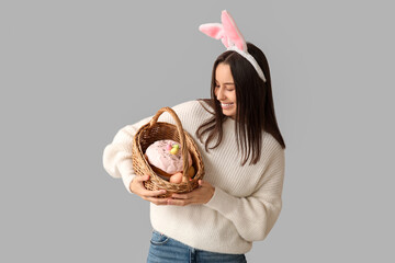 Poster - Pretty young woman with bunny ears and Easter basket on grey background