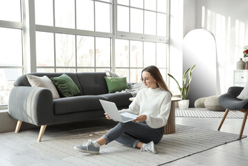 Wall Mural - Young woman using laptop near window in living room