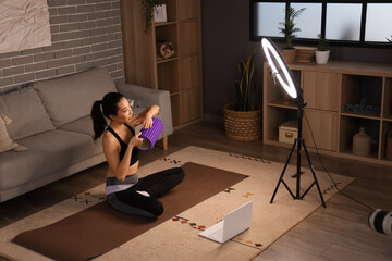 Wall Mural - Female Asian sports blogger with foam roller recording training video at home