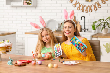 Poster - Cute little girl and her happy mother in bunny ears painting Easter eggs in kitchen