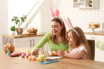 Poster - Cute little girl and her mother in bunny ears painting Easter eggs in kitchen