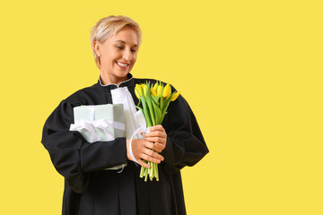 Canvas Print - Mature female judge with tulips and gift on yellow background. International Women's Day celebration