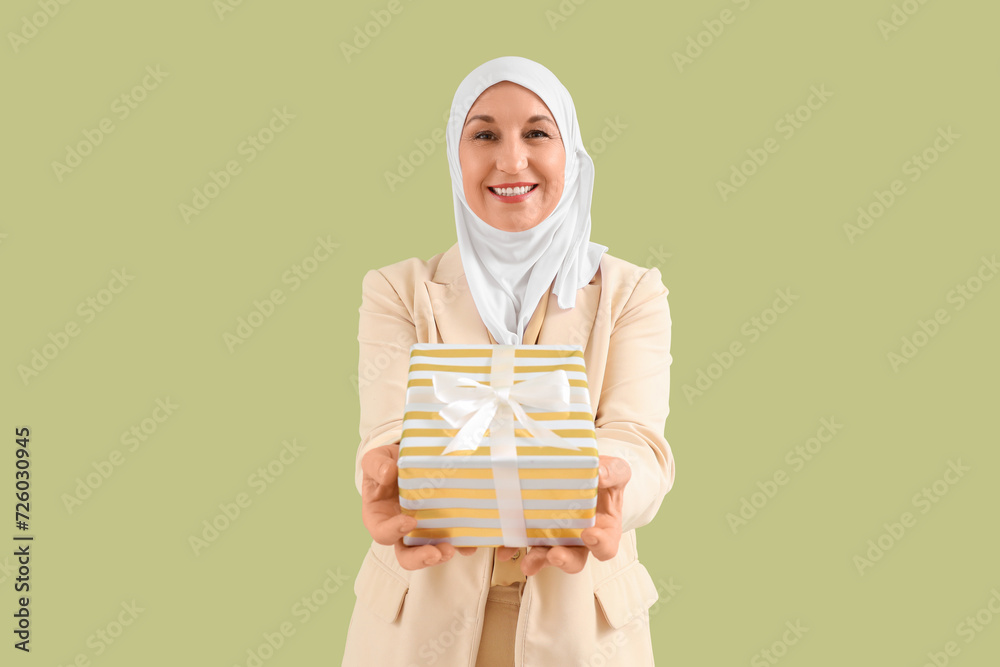 Mature Muslim woman with gift box on green background. Ramadan celebration