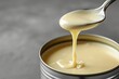 Closeup of condensed milk being poured into a tin can on a grey background