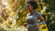 © mariiaplo - Joyful pregnant woman maintaining fitness with a morning run in the park.