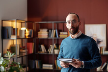 Medium Portrait Of Young Middle Eastern Psychotherapist With Beard On Face Standing In Office With Notebook And Pen In Hands Looking At Camera