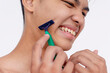 A young asian man nicks his skin while using a disposable razor to cleanly shave the sideburns. Possible cut on the face. Closeup tight shot isolated on a white backdrop.