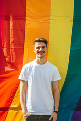 Young gay man wearing a blank white mockup t-shirt in front of a giant gay rainbow flag