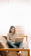 © Yauhen - Joyful millennial woman typing on a laptop, attending a virtual meeting, seated on a sofa. Cheerful millennial female typing on laptop, has meeting with gadget, sit on sofa.