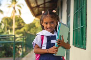 A smiling young student in a uniform, carrying books, exemplifies eagerness and education in a tropical setting.