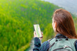 Young woman uses smartphone at sunny mountains and using travel app or map during her hike. Empty space for text